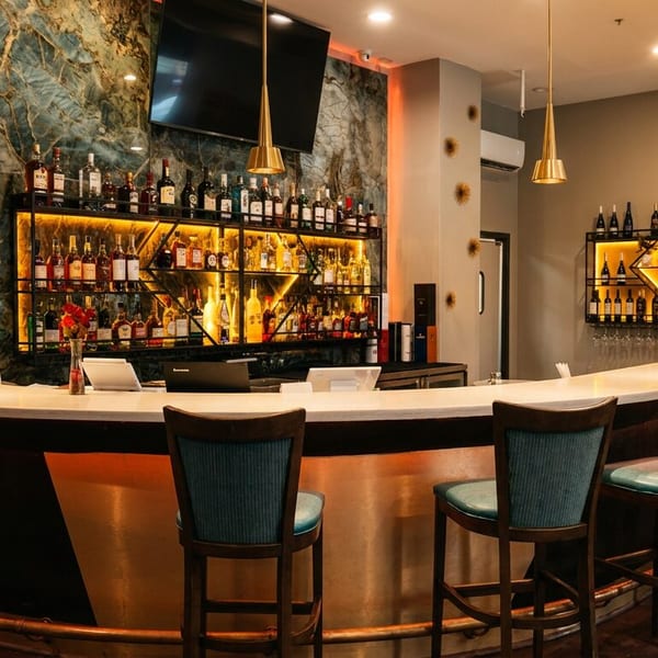 Elegant bar area with a long counter, blue stools, and illuminated shelves of bottles.