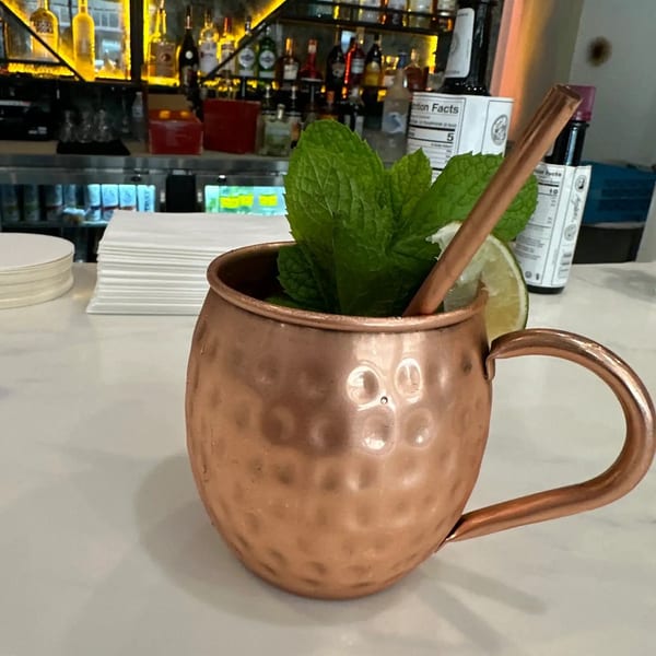 A copper mug with a cocktail, garnished with mint and lime, sits on a bar.
