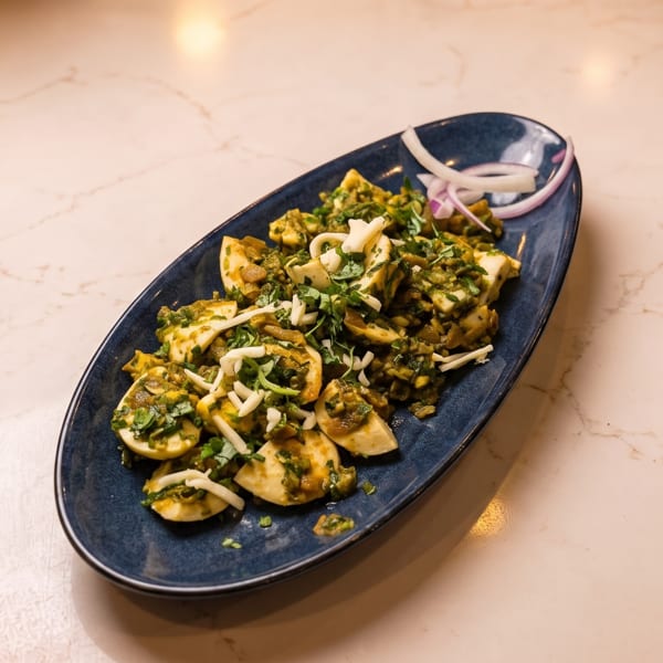A blue oval plate filled with deviled eggs topped with green relish, shredded cheese, and red onion.
