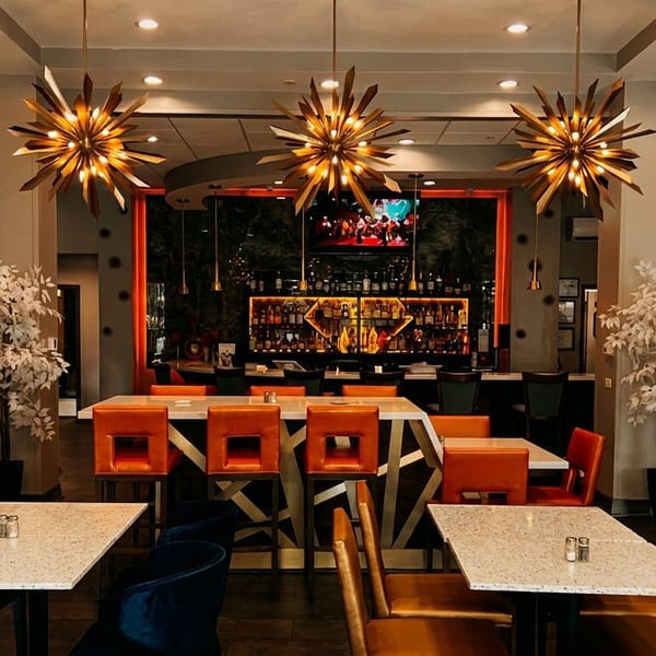Restaurant interior with orange and blue seating, starburst chandeliers, and a well-stocked bar.