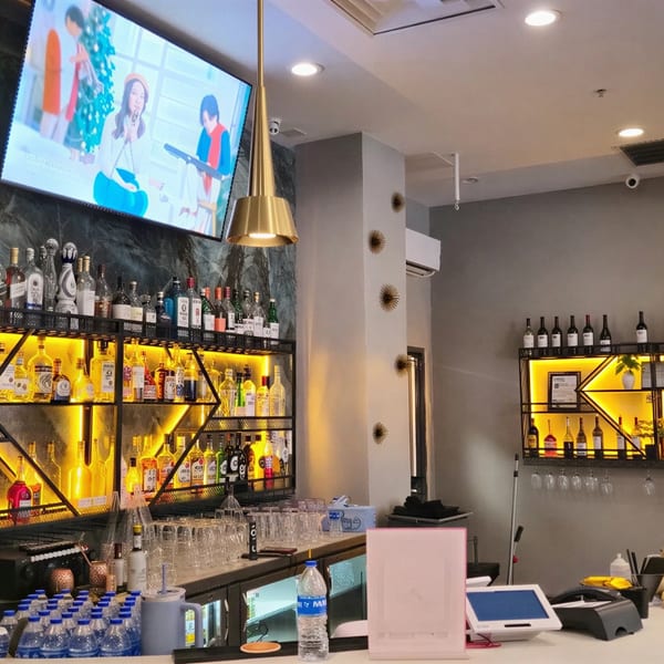A modern bar with illuminated shelves displaying liquor bottles, a TV, and gold pendant lights.