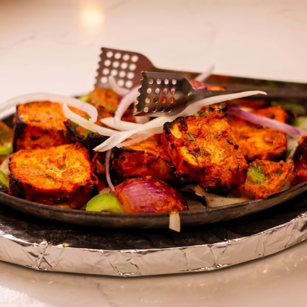 Sizzling paneer tikka with onions and peppers in a cast iron pan on a marble surface.