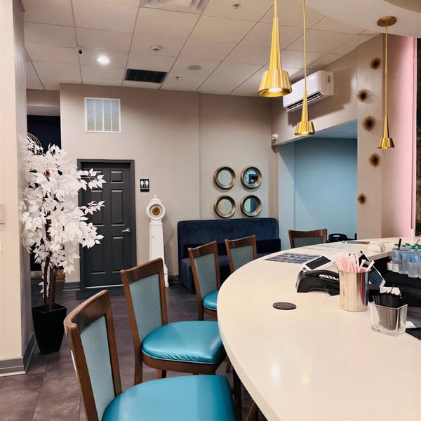 A modern restaurant interior with a white bar, teal bar stools, and gold pendant lights.