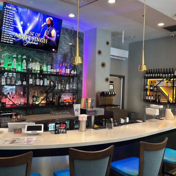 A well-stocked bar with a large TV displaying a music playlist, and modern pendant lights.