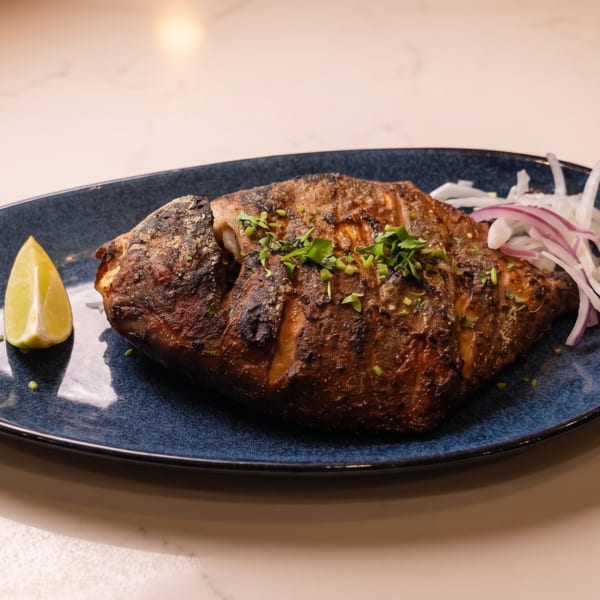 Whole grilled fish garnished with parsley, sliced onions, and a lime wedge on a blue plate.